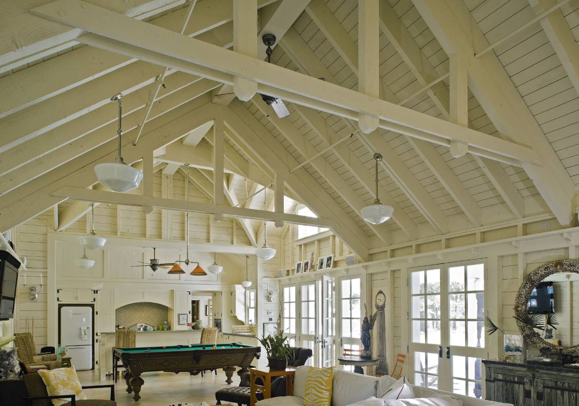 Clerestory windows, multiple french doors, whitewashed open truss ceiling, and schoolhouse lights evoke a vacation home at the beach.