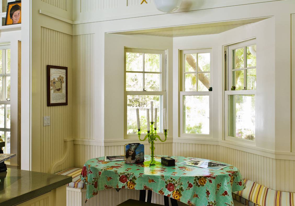 Custom double hung windows frame views at this cozy bay in the kitchen with built-in bench seating and seaside accents.