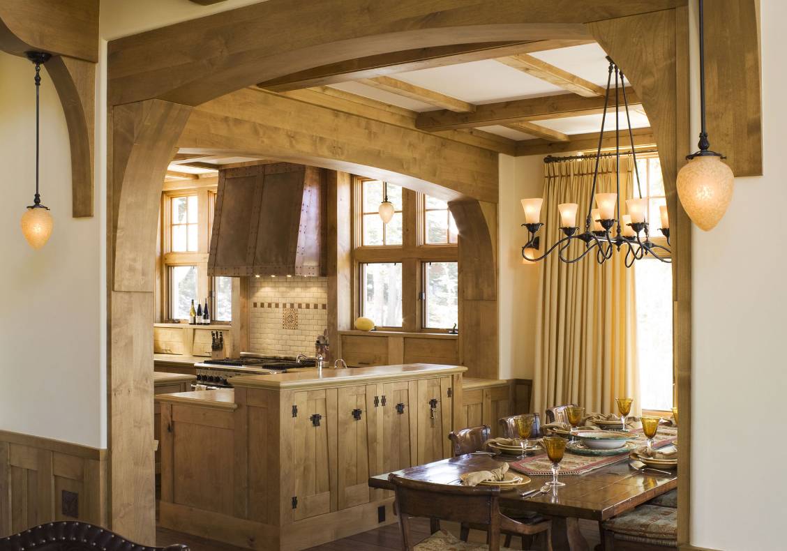 Stained alder wood frames the entry to the dining area of this art nouveau mountain home, with art glass pendant lights hanging from an interior balcony.
