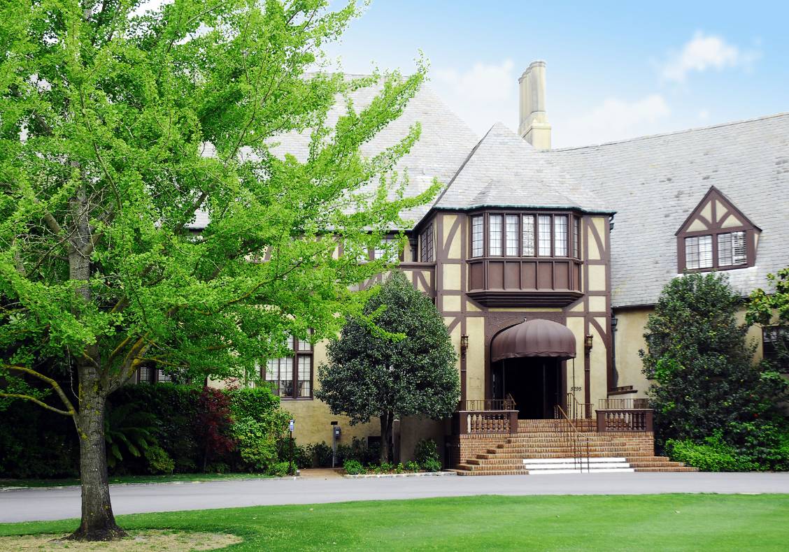 A beautiful, full green tree frames the peaceful main entrance to the country club, which is graced by a wooden balustrade and brick steps that cascade down to the main walkway.