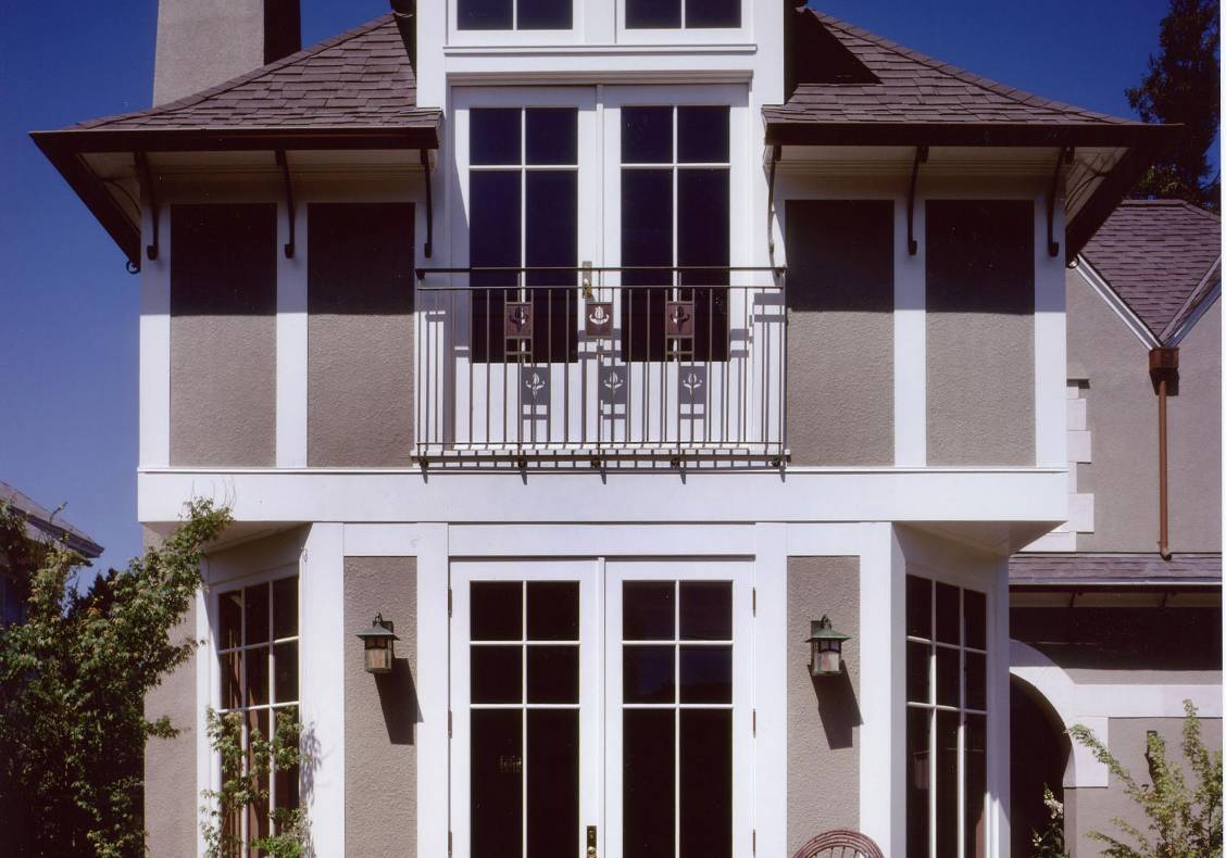 Voysey-inspired details include hammered iron soffit brackets, waterjet cut railing details, rendered walls with white trim, and hip dormers.
