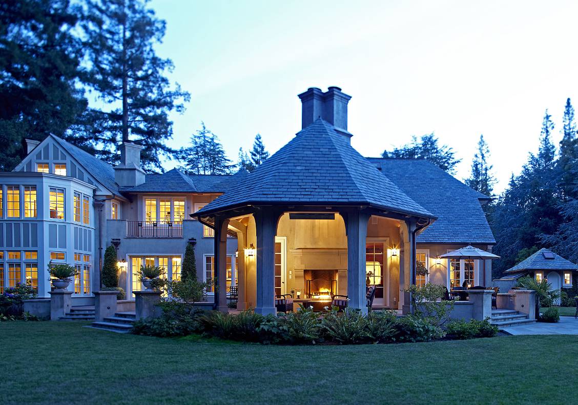 Outdoor room with heavy timber frame, fireplace, slate roof, Lutyens chimney caps, evening view.