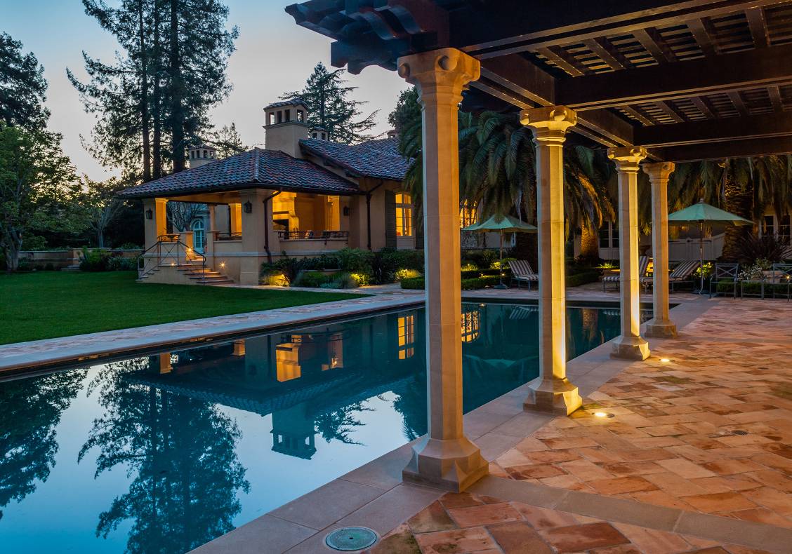 This pool house takes its stylistic cues from the main residence, with thick, stucco-finished walls, stone trims, and a Roman tile roof.