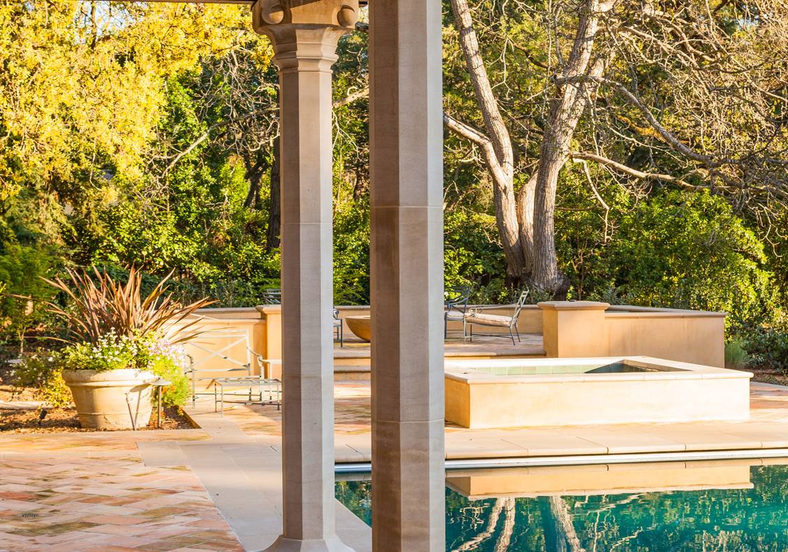 A wooden trellis on stone columns provides shade next to the pool.