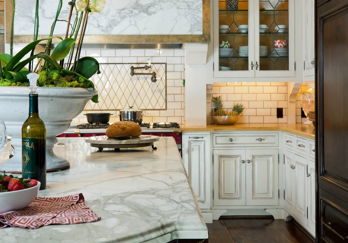 The Carrara Calacata marble top island is a counterpoint to the warm Jerusalem gold counters beneath creamy painted cabinets supported by ovulo wooden brackets.