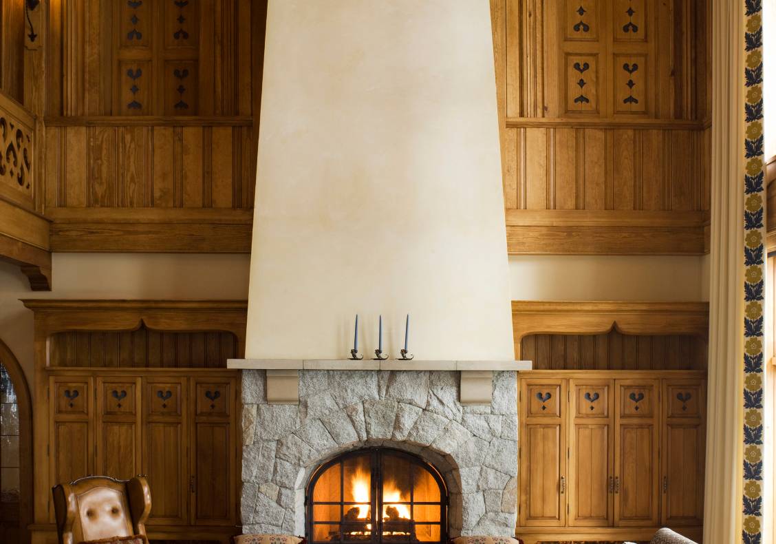 The fitted stone mantel supports a chimney that climbs two storeys to the pine ceiling.