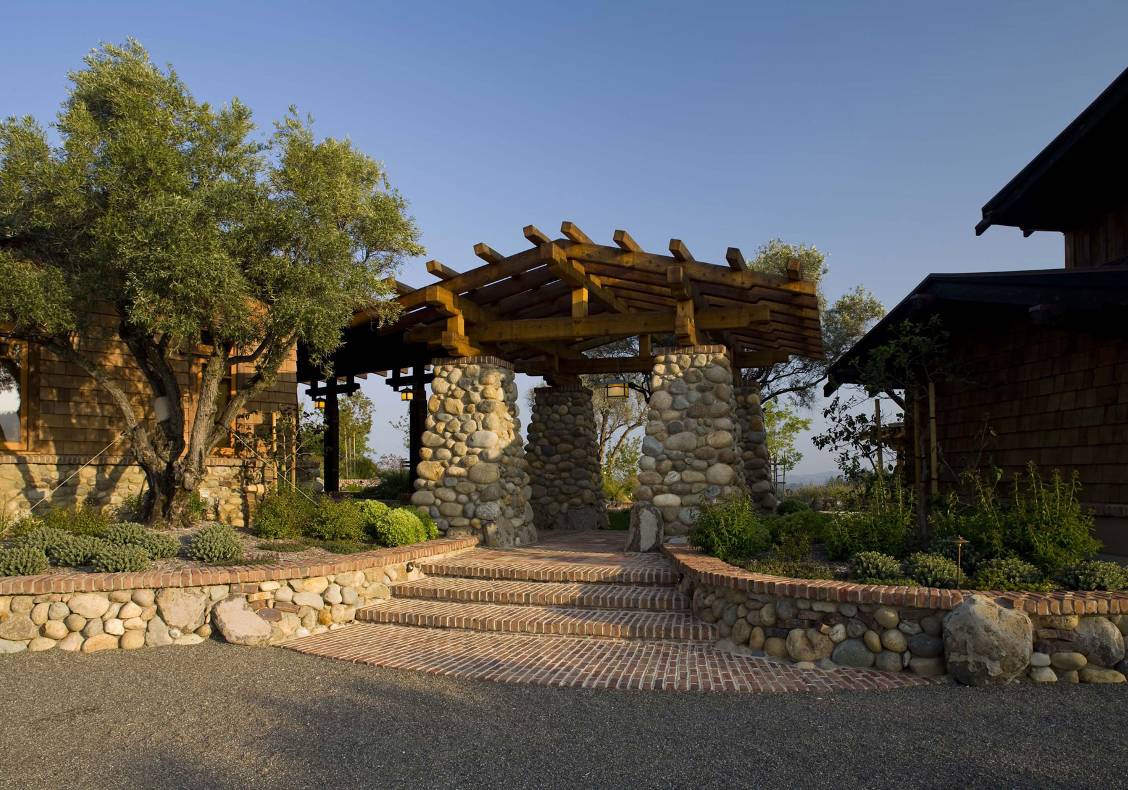 A massive stone entry pergola with reclaimed brick and stone walkway announce the entrance to the home.